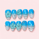 Azure Shell short almond press-on nails in bright blue fading to silver glitter with sculpted mint flowers and bead strands
