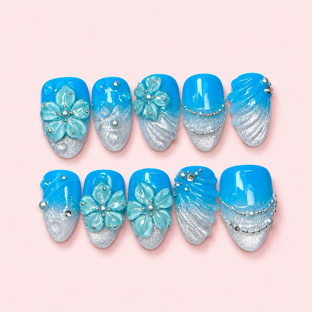 Azure Shell short almond press-on nails in bright blue fading to silver glitter with sculpted mint flowers and bead strands