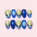 Cobalt Dot short almond press-on nails in cobalt blue and pale sage with white dots and gold-toned frames