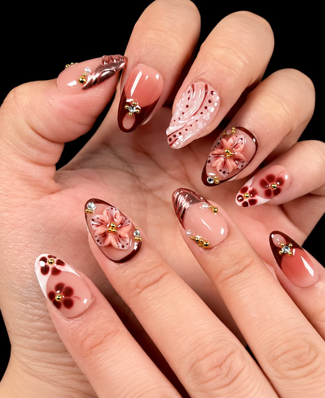 Brown French tip short nails with color, featuring floral details, pearls, and gold accents worn on the hand.