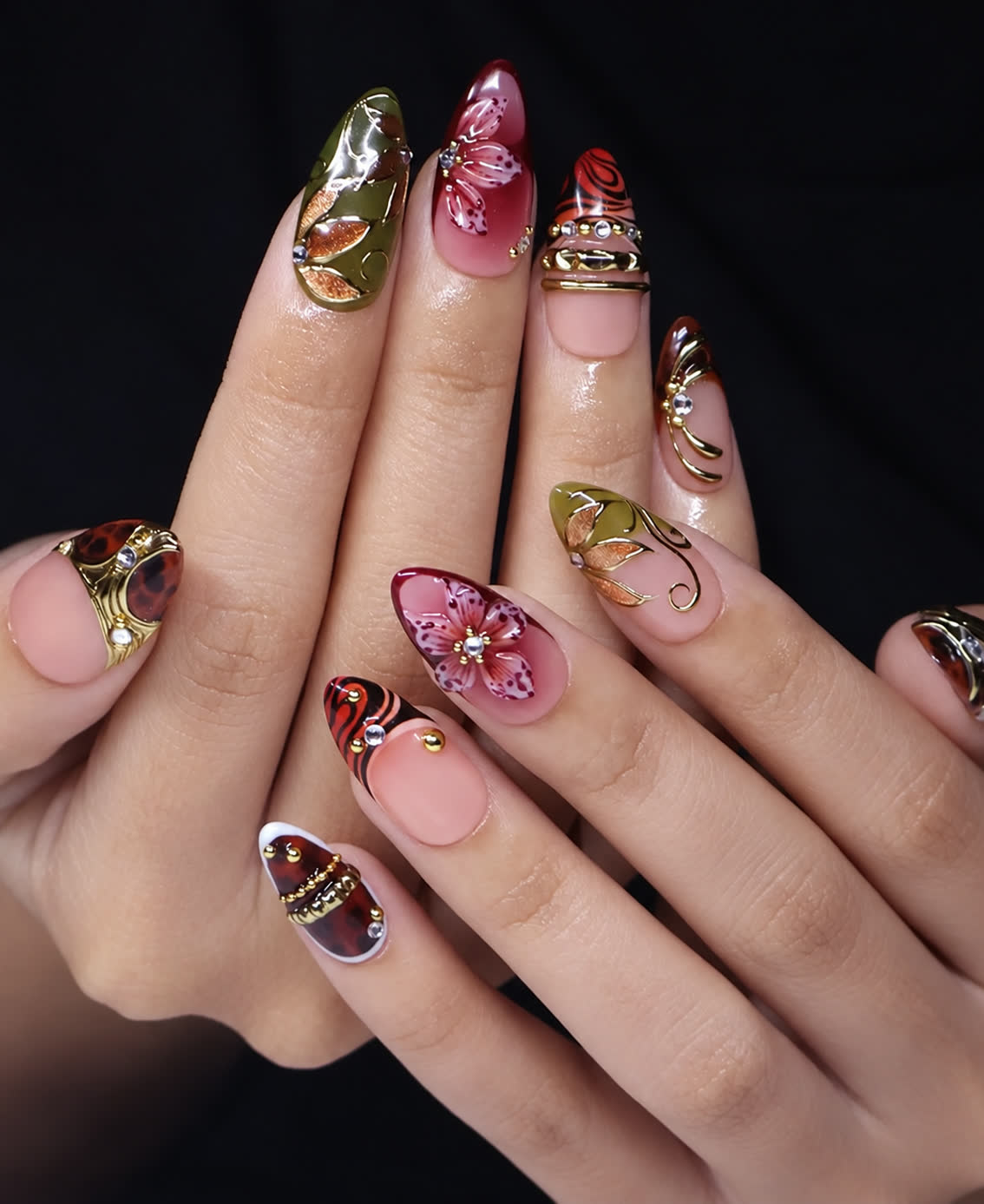 Close-up of short almond nails with 3D burgundy flowers, olive leaf details, gold beads, gemstones, and animal print tips.